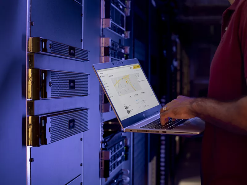 A person holding a laptop in a dark server room.